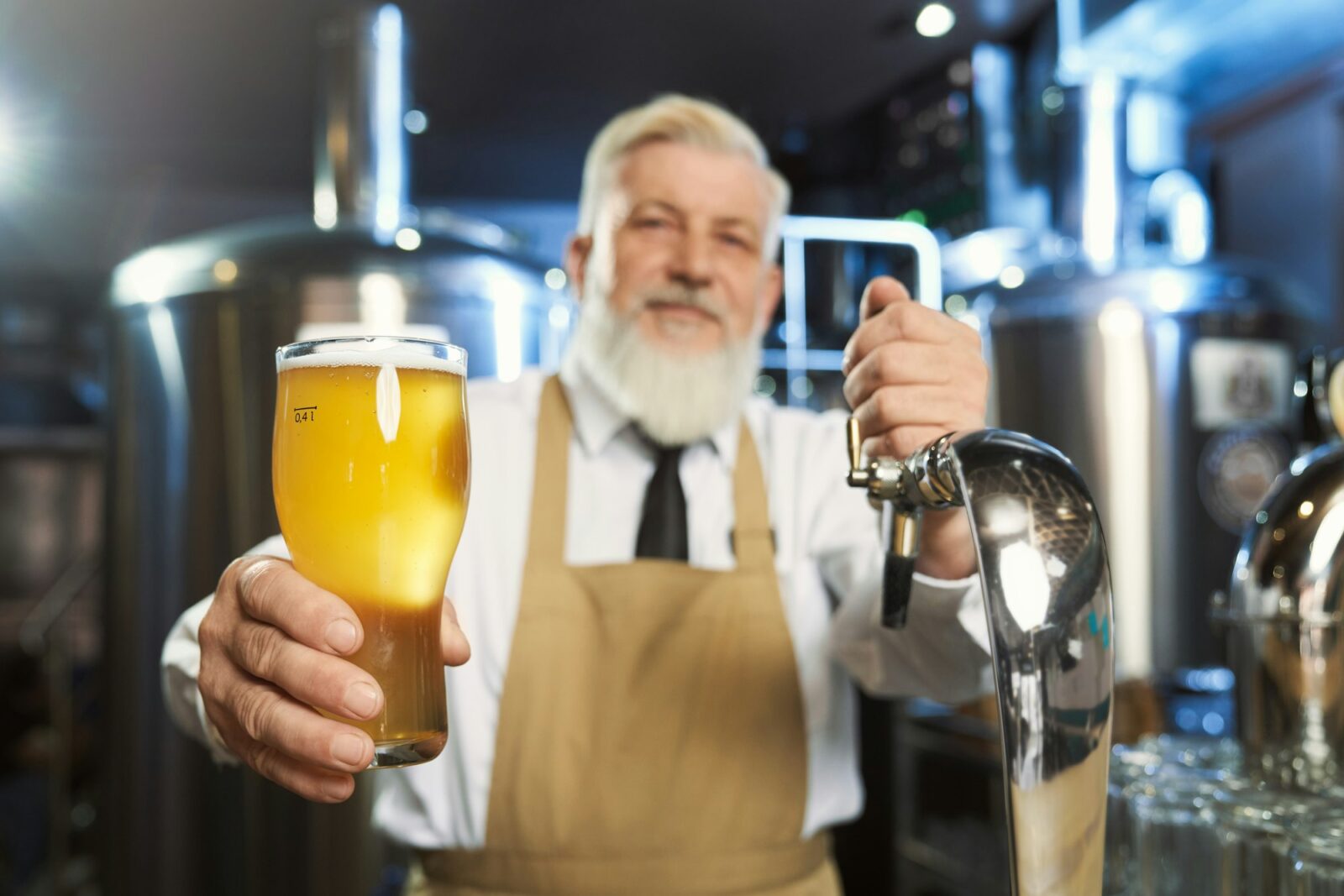 Elderly barman holding cold glass with lager beer