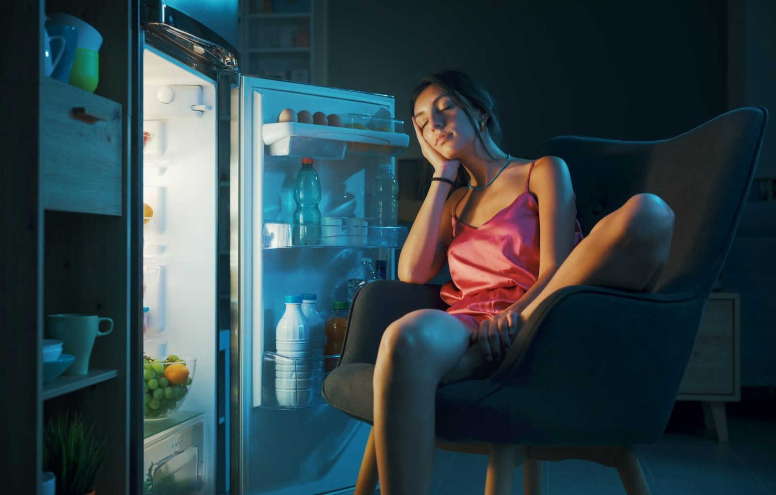 Woman suffering from the heat and sitting in front of the open fridge
