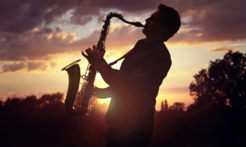 Saxophonist playing sax against sunset