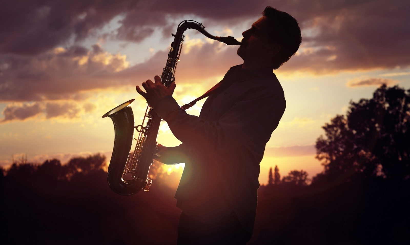Saxophonist playing sax against sunset